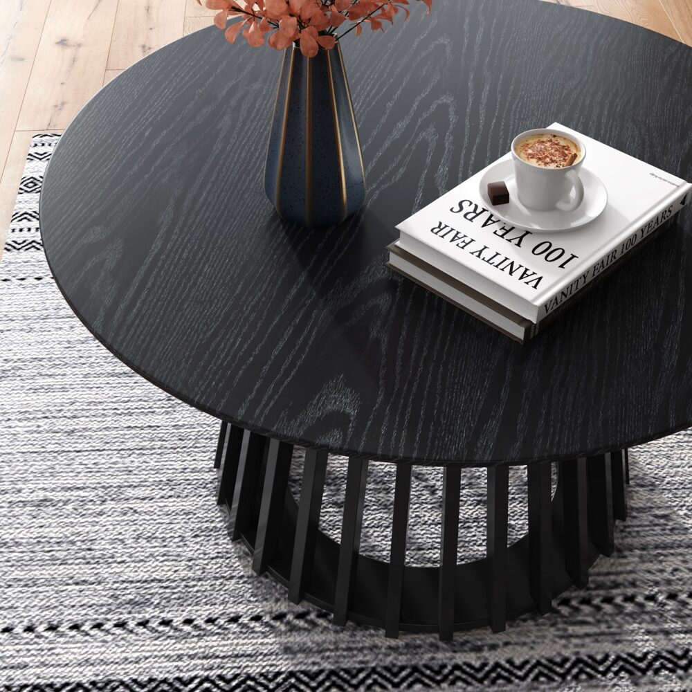 Black round coffee table with slatted pedestal base styled in a living room with a vase of flowers, books and coffee cup on