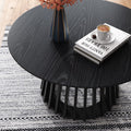 Top-down view of a black round coffee table showing a vase of orange flowers, stacked books and a coffee cup