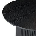 Close-up side-angle of black round coffee table showing wood grain texture of top surface and fluted base edge