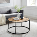Round coffee table with sunburst wood top and black metal frame in living room with grey sofa, vases and cup on top