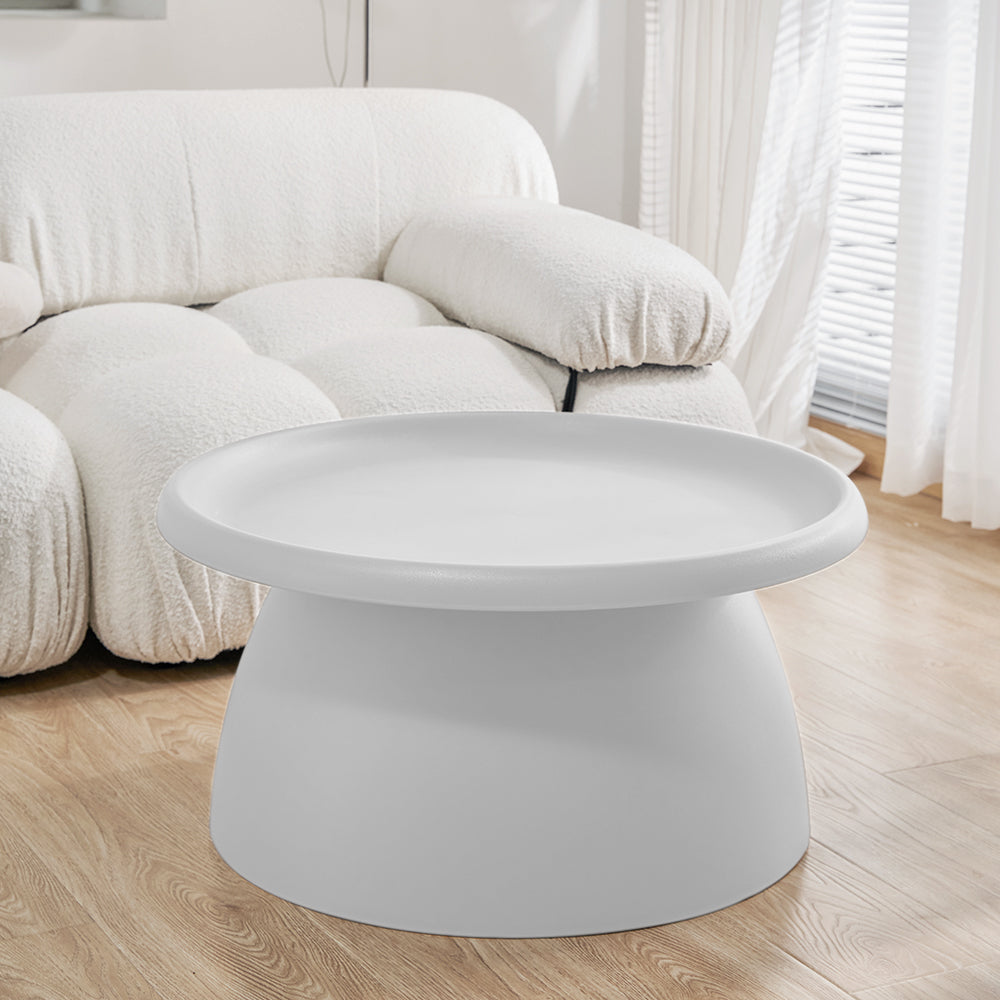 Round white coffee table with wide tray top and tapered cylindrical base in a living room with a bouclé sofa and timber floor