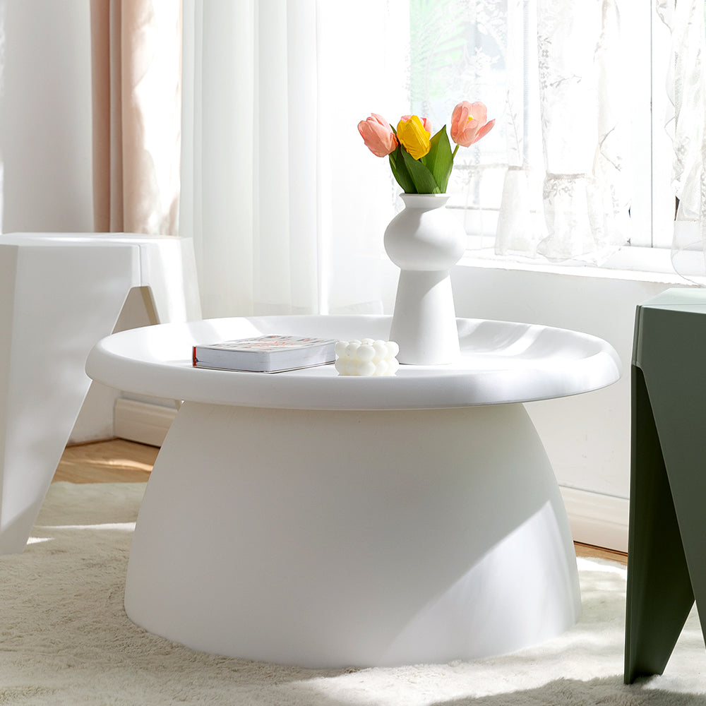 Round white coffee table with tray top styled with a vase of tulips, a book and a candle ornament near a window in a bright
