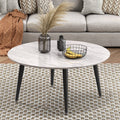 Round coffee table with white marble-effect top and black tapered legs styled in living room with sofa and rug
