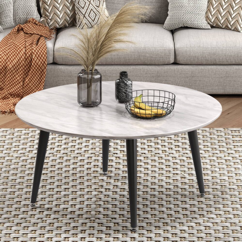 Round coffee table with white marble-effect top and black tapered legs styled in living room with sofa and rug