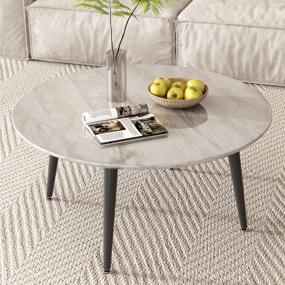 Round marble-effect coffee table viewed from above with open magazine, fruit bowl and glass vase on woven rug