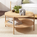 Cylindrical hammered brass-finish metal coffee table on weathered timber floorboards against a white concrete wall, angle