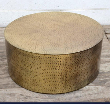 Cylindrical hammered brass-finish metal coffee table front view with concentric circle hammer pattern on the top surface,