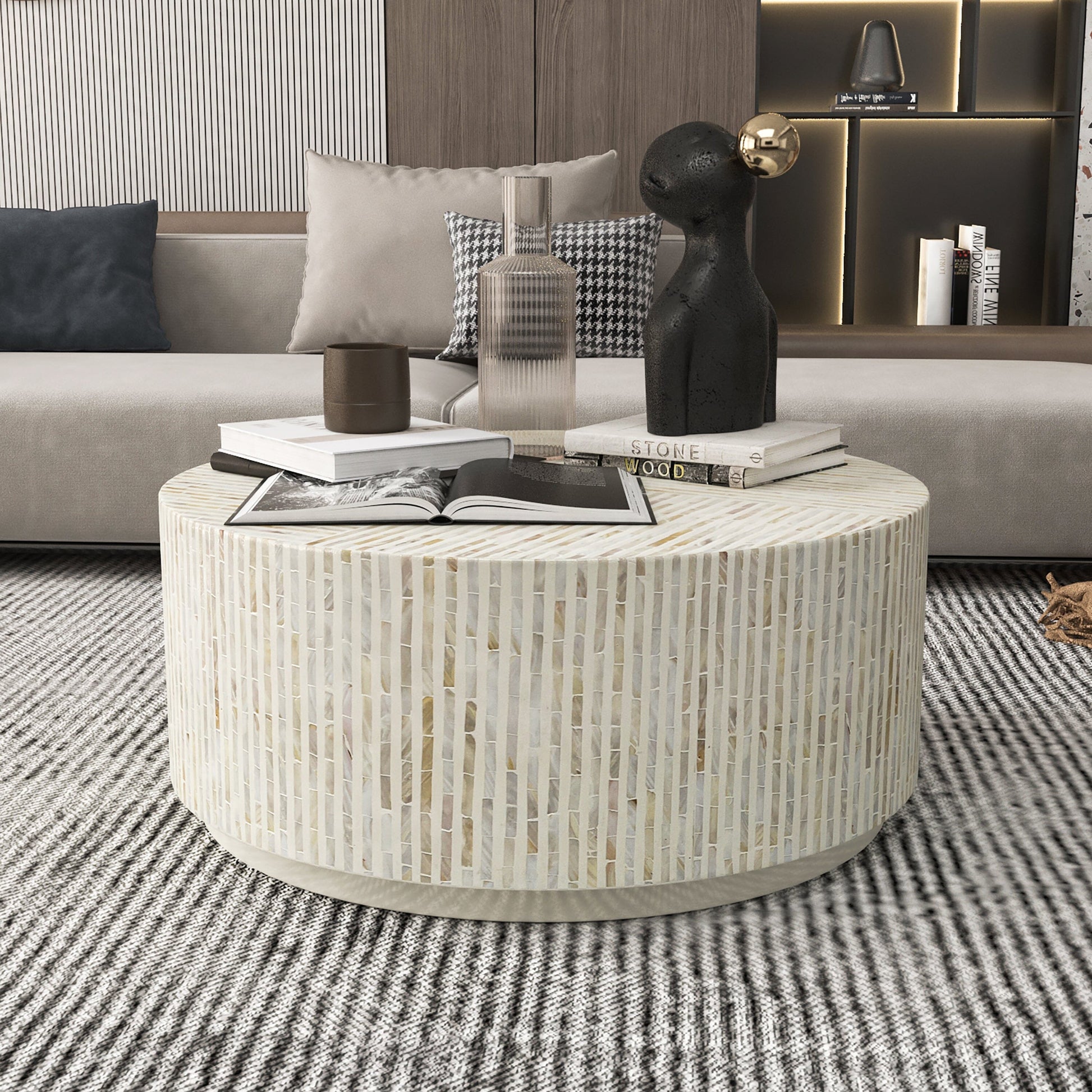 Round drum coffee table with mother of pearl mosaic tile surface in white and beige, styled with books in a living room