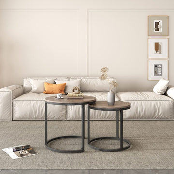 Two round nesting coffee tables with walnut-look tops and dark metal bases in front of cream sofa, framed art on wall