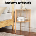 Round two-tier oak side table with rope spindle sides placed beside a bed with books stored on the lower shelf