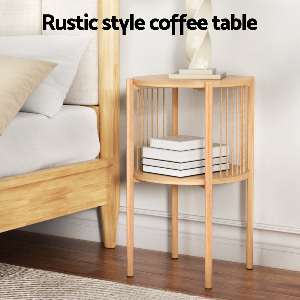 Round two-tier oak side table with rope spindle sides placed beside a bed with books stored on the lower shelf