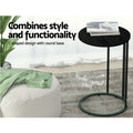 Round black C-shaped side table with powder-coated steel base callout, magazine on top, pouf and plant beside, living room