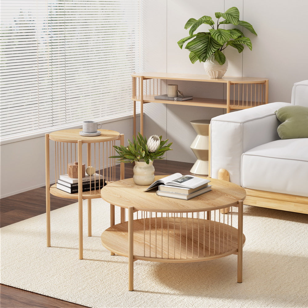 Round two-tier natural oak coffee table in front of a white sofa, with a coffee cup, plant vase and books on the table