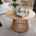 Round natural pine coffee table with splayed slatted wood pedestal base, styled in a living room with white tulips, books