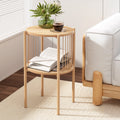 Two-tier round natural oak side table at angle view with an open book and magazine on lower shelf and a coffee cup and plant