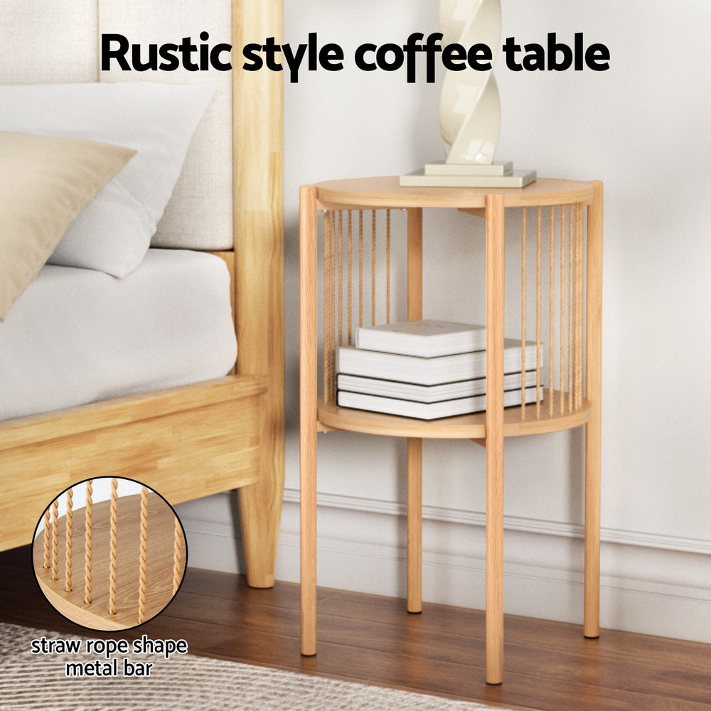 Round two-tier natural wood side table with twisted metal bar spindles, styled beside a bed with books on lower shelf and