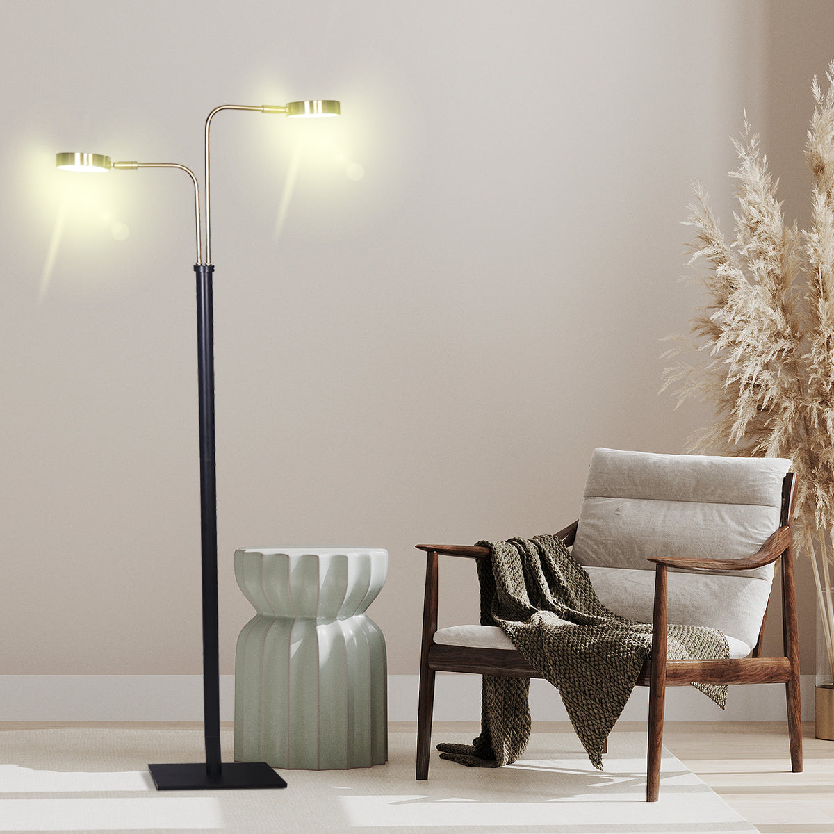Dual-arm LED floor lamp lit in a beige room beside a ceramic stool, wooden armchair with throw and pampas grass