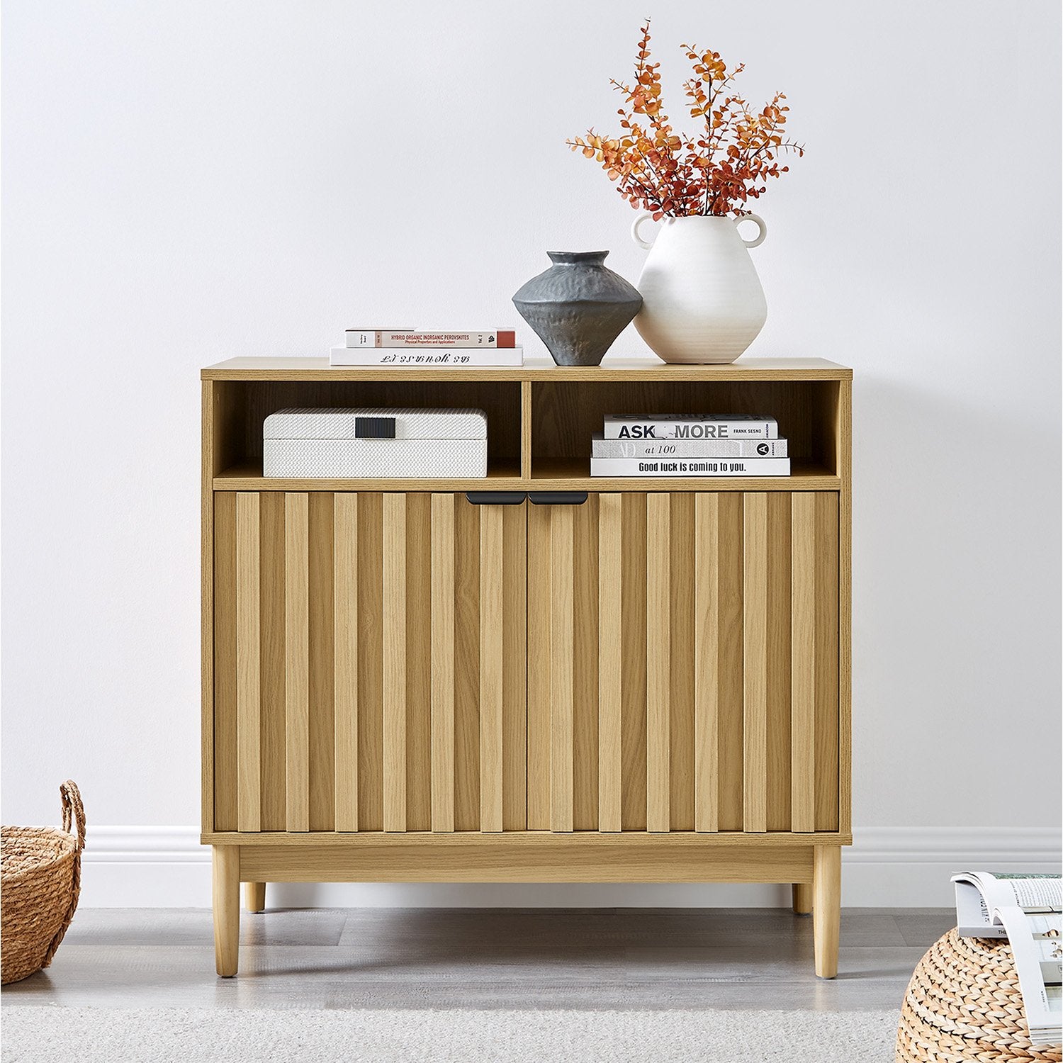 Sarantino Eleni sideboard in room setting, router and books in open niches, vases and foliage on top, wicker baskets on floor