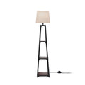 Floor lamp with beige empire shade on tapered black open-frame base with two shelves on white background