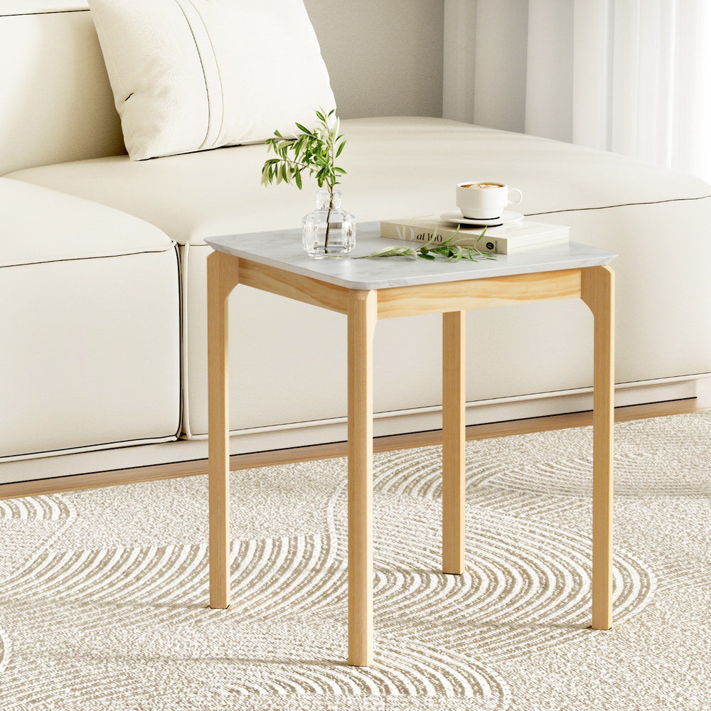 Square side table with white marble-effect top and natural wood legs beside cream sofa on patterned rug