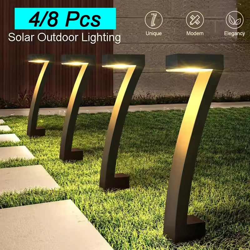 Three arch solar bollard lights glowing warm on grass beside stepping stone path at night, modern house wall in background
