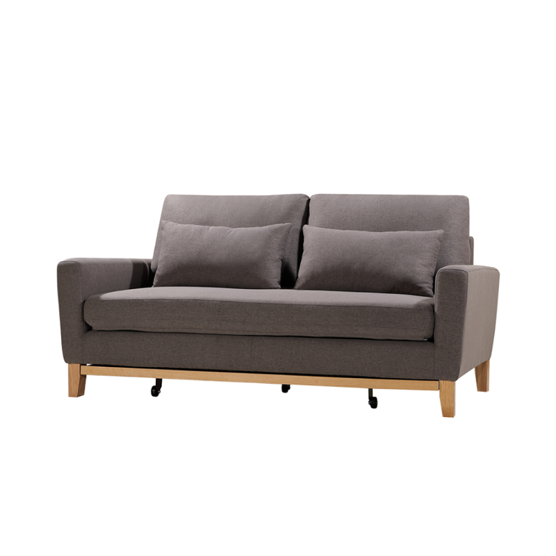 Angle view of taupe fabric sofa bed with two scatter pillows and wood legs with casters on white background