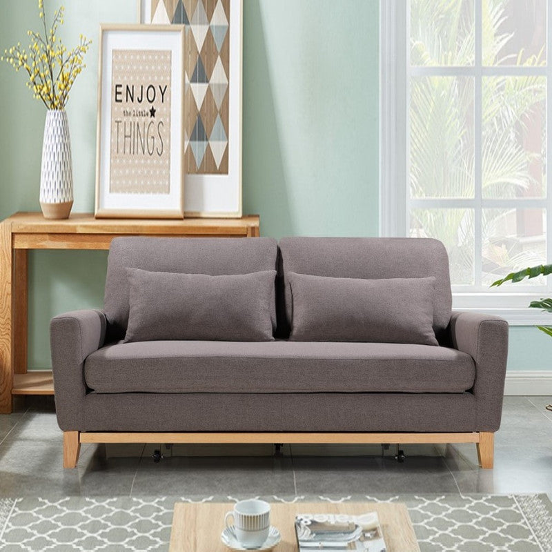 Taupe fabric sofa bed fully extended showing white mattress, two scatter pillows and wood frame with casters
