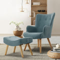 Teal velvet button-tufted wingback armchair with matching tufted footstool, in room with pendant lamps and wooden shelf