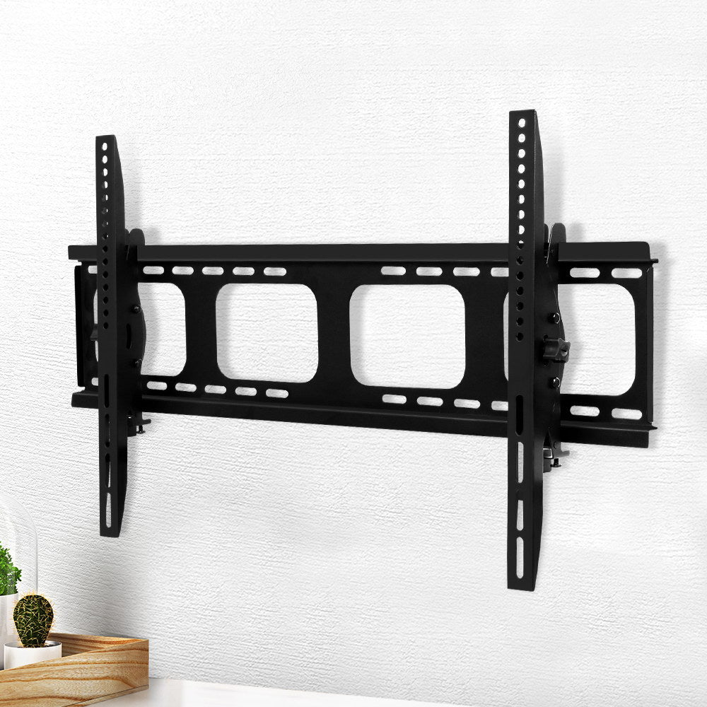 Black tilting TV wall bracket on white textured wall lifestyle with cactus and plant on wood tray in bottom corner