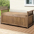 Brown timber outdoor storage bench on patio deck with woven rug, weatherboard house wall and trees in background