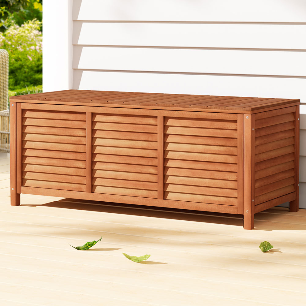 Honey timber outdoor storage box with louvred three-panel sides on deck, white weatherboard wall in background
