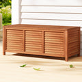 Honey timber outdoor storage box with louvred three-panel sides on deck, white weatherboard wall in background