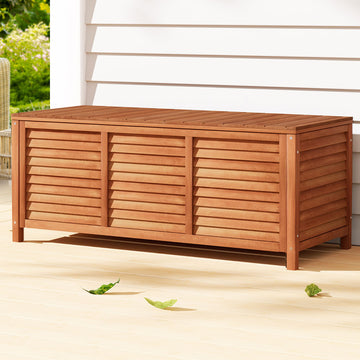 Honey timber outdoor storage box with louvred three-panel sides on deck, white weatherboard wall in background