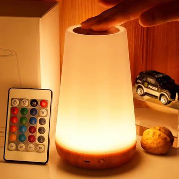 Conical white LED lamp with wood-grain base glowing warm, hand on top; RGB remote with colour buttons, timers and ON/OFF