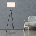 Tripod floor lamp with white drum shade beside a light blue armchair in living room with concrete wall