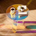Iridescent acrylic round side table viewed from above on timber floor with a coffee cup, stacked books and small cactus on