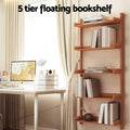 Wall-mounted ladder shelf loaded with books styled beside a desk in a bright home study; text reads 5 tier floating bookshelf