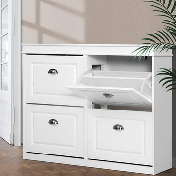 White wide four-door shoe cabinet top-right flip-out tray open showing mechanism in hallway with palm plant and natural light