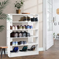 White 5-tier shoe rack loaded with sneakers leather shoes and sequin heels in hallway herringbone floor palm plant and door