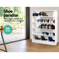 White 5-tier shoe rack loaded with boots heels and sneakers shoe paradise 30 pairs text deck visible through glass door