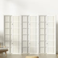 White 6-panel grid pattern shoji room divider in lifestyle room against white wall with wooden chair and floor cushion