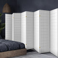 White 8-panel fabric grid room divider in bedroom lifestyle with charcoal bedding rattan pendant lamp and palm plant