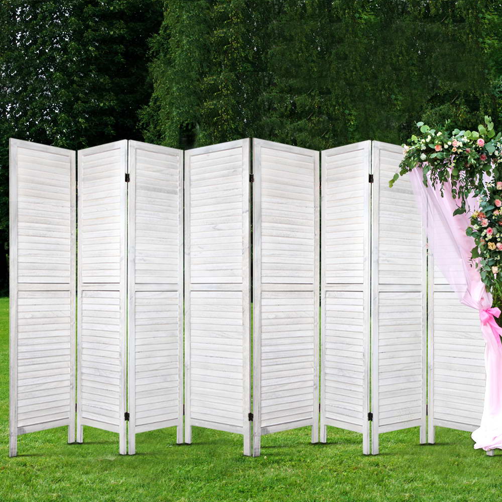 White 8-panel louvered wood room divider outdoors in garden with green grass and pink floral arch drapery