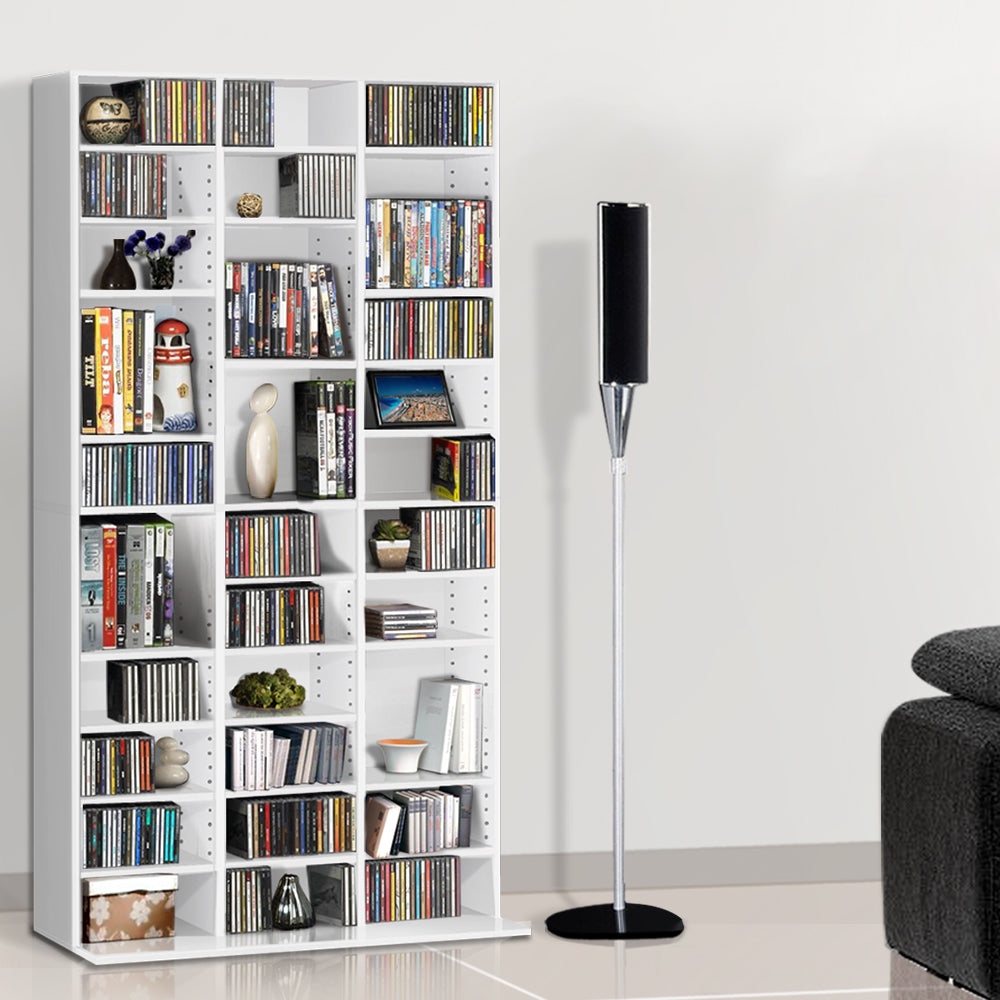 White multi-column CD and DVD media storage shelf loaded with discs and books in living room beside speaker