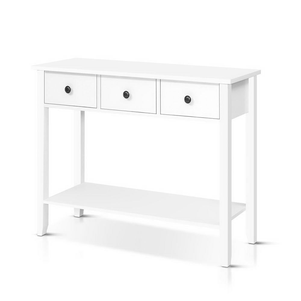 White console table with three drawers, black round knobs, bottom shelf and flared legs, white background
