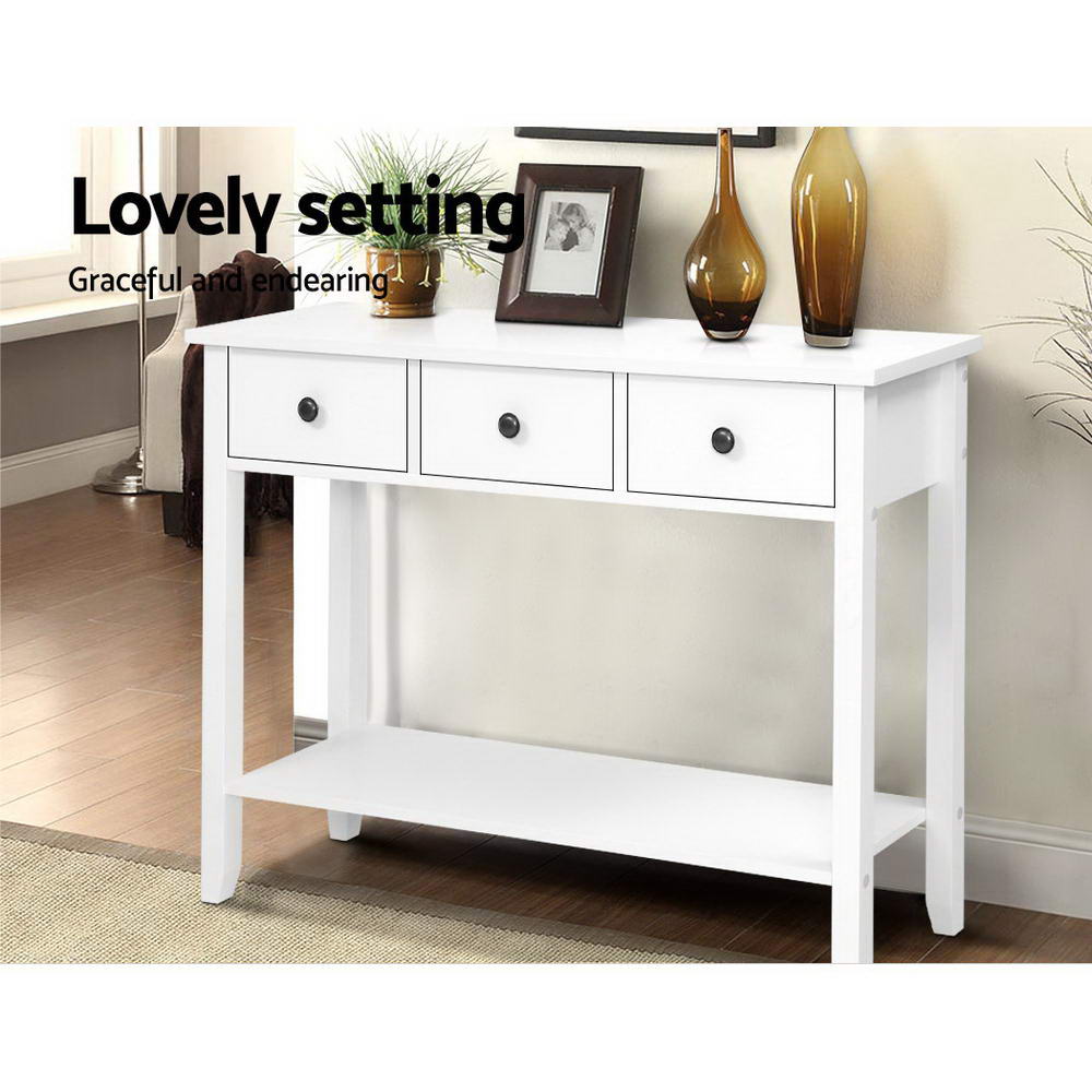 White 3-drawer console with bottom shelf in hallway; styled with plant, photo frame and amber vases; text "Lovely setting"