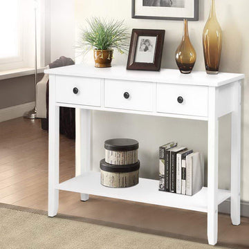 White console table with 3 drawers and bottom shelf in room; styled with plant, photo frame, amber vases, and books on shelf