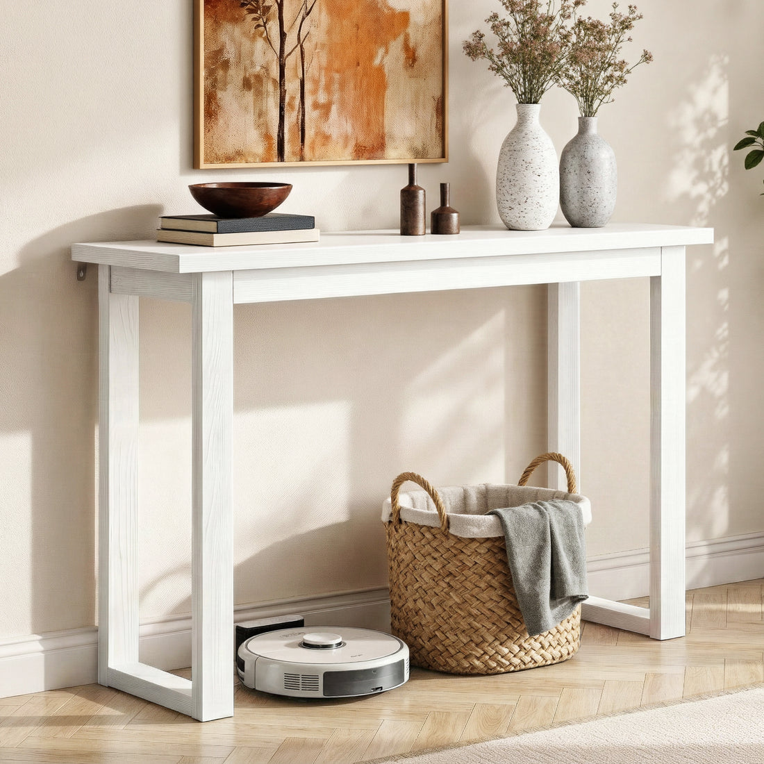 White console table in hallway styled with speckled vases and dried flowers on top, wicker basket and robot vacuum under