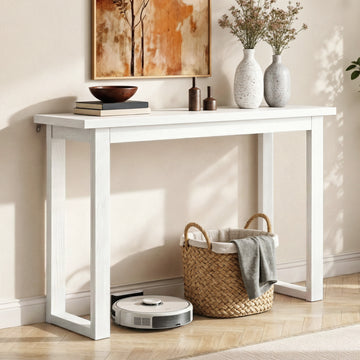 White console table in hallway styled with speckled vases and dried flowers on top, wicker basket and robot vacuum under
