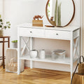 White console table with two drawers, X-frame sides and lower shelf, styled with vases and rhino figurines in entryway